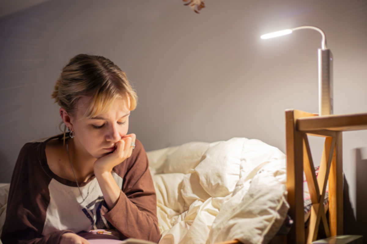 Young woman reading in bed under a soft light as part of a calming bedtime routine before taking melatonin