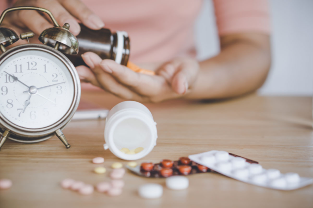 Melatonin Timing and Dosage Routine – Vitasunn Nutritionals Person taking supplements beside a clock as part of a timed bedtime melatonin routine